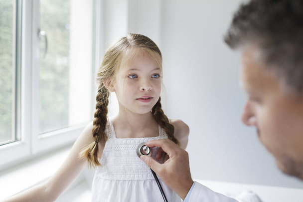 male doctor in white coat examines young, pretty girl in his practice - Фото, зображення