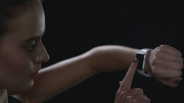 Spor kadını siyah arkaplanda akıllı saat ekranına dokunuyor - Fotoğraf, Görsel