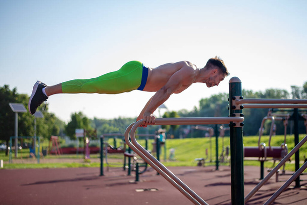 Caucasian young man outdoor at park at city.  Serious caucasian sportsman training topless outdoors on horizontal bar keeping healthy lifestyle  male athlete doing exercises for arms. The sport, fitness, health, lifestyle concept. - Φωτογραφία, εικόνα