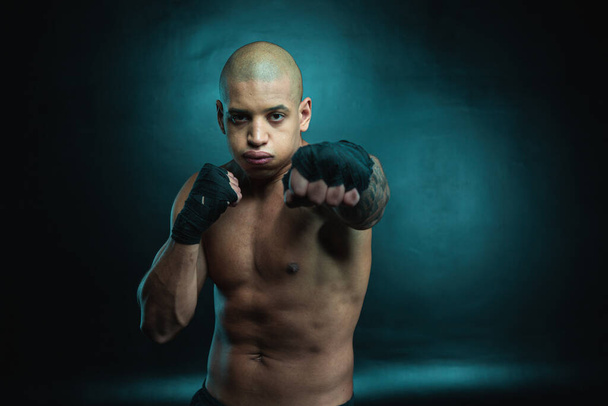 Confident professional fighter standing shirtless with bandages on the hands and putting one fist forward - Foto, Imagen