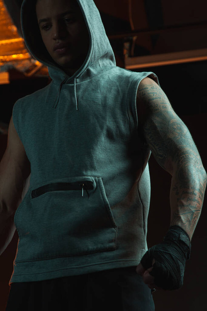 М'язистий татуйований молодий чоловік має боксерську пов'язку на руці, стоячи один і стискаючи кулак
 - Фото, зображення