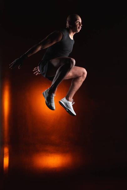 Confident professional athlete looking away while jumping high on the orange light background - Foto, Imagen