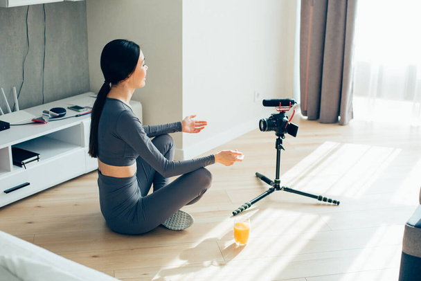 Long haired pretty lady sitting on the floor in a lotus pose and recording a video for her blog - 写真・画像