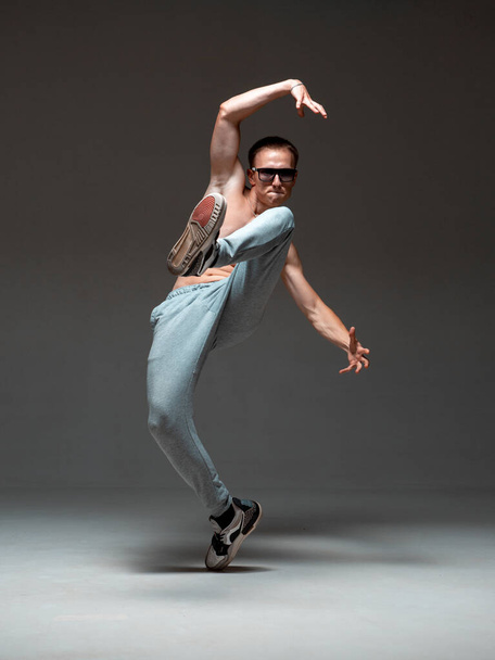 Um tipo fixe, um breakdancer de óculos de sol, a dançar hip-hop sem camisa no estúdio. Cartaz da escola de dança. Aulas de dança de pausa
 - Foto, Imagem