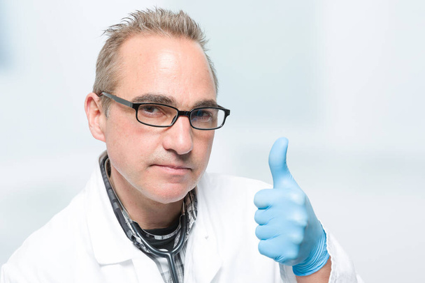 mannelijke arts in de voorkant van een kliniek kamer toont duimen omhoog - Foto, afbeelding