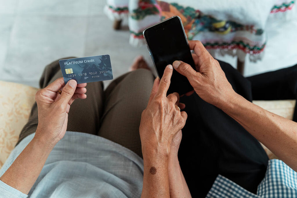 Close up mãos de idosos asiáticos casal segurando smartphone e cartão de crédito. Compras online de Transferir dinheiro para outra conta
. - Foto, Imagem