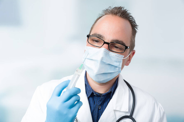 médico masculino con mascarilla médica manejando una jeringa delante o - Foto, Imagen