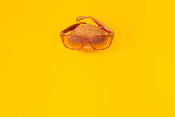 a coconut in sunglasses on yellow background. The concept of relaxation, summer mood - Photo, Image