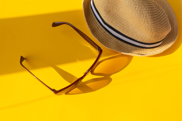 Strohhut und Sonnenbrille auf gelbem Hintergrund mit Schatten. Farbkonzept von Reisen oder Urlaub. - Foto, Bild
