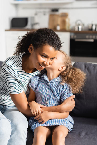 african american girl whispering in ear of mother while sitting on sofa at home - Foto, Imagem