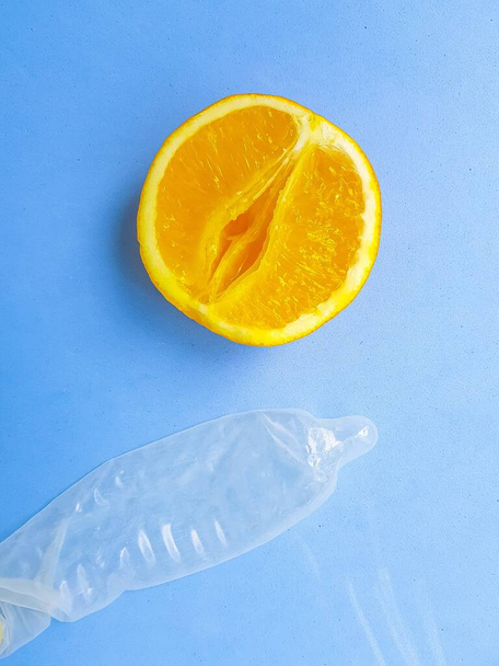 The concept of safe sex and protection. A vagina symbol. A juicy orange and a condom on a bright blue background. - Fotografie, Obrázek