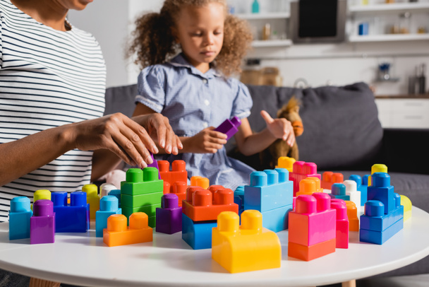 cropped view of african american babysitter and child playing with multicolored building blocks together - Foto, afbeelding