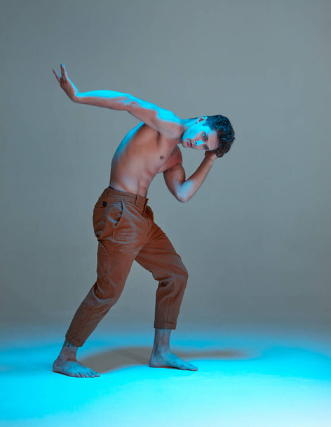 Cool young man dancer dancing without shirt in neon blue light in studio. Dance school poster - Фото, зображення