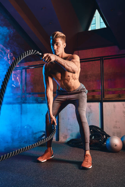 Man with battle rope battle ropes exercises in fitness gym. Cross Fit concept. - Zdjęcie, obraz