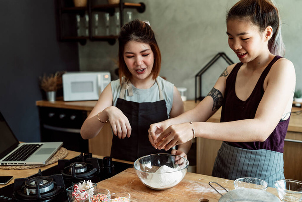 大きなガラスのボウルの中に小麦粉に卵を割る2人の若いアジアの女性,それを混ぜる準備ができて.. - 写真・画像
