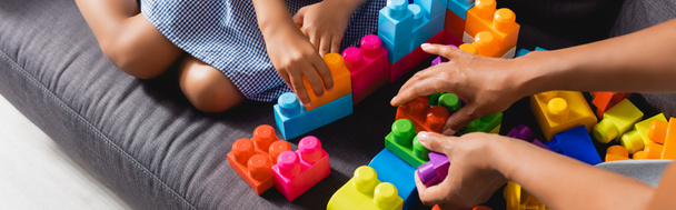 cropped view of african american babysitter and girl playing with multicolored building blocks, panoramic shot - Foto, Imagen