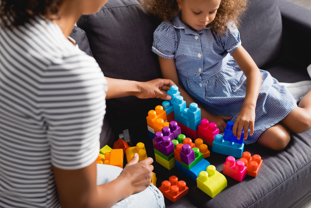 cropped view of babysitter near african american girl in dress playing with multicolored building blocks  - Фото, изображение