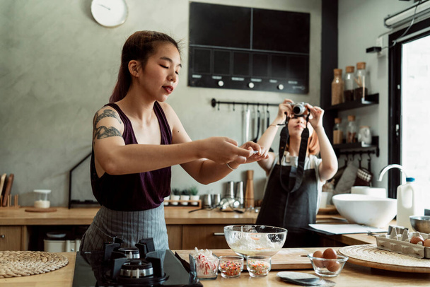 dos asiático panadero mujeres tomando un foto de harina dentro el cuenco mientras otro chica grabación vídeo con cámara. - Foto, Imagen