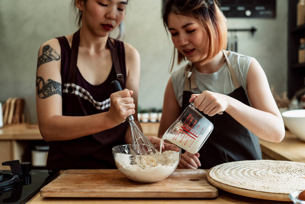 Дві азіатські пекарні змішують борошно, молоко, яєчний жовток у скляній мисці разом на кухні. Процедура приготування хліба
. - Фото, зображення