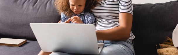 cropped view of african american teleworker in striped t-shirt using laptop near upset daughter, horizontal image - Fotoğraf, Görsel