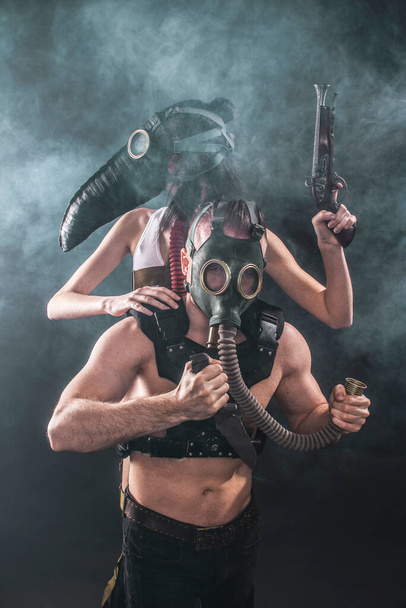 A girl in a plague mask and a guy in a gas mask holds a knife in his hands. against the background of smoke - Photo, Image