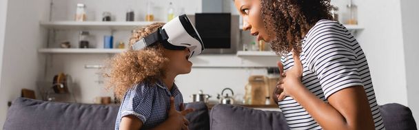 animado afro-americano babá e criança no vr headset segurando as mãos sobre os peitos enquanto olhando um para o outro, tiro panorâmico - Foto, Imagem