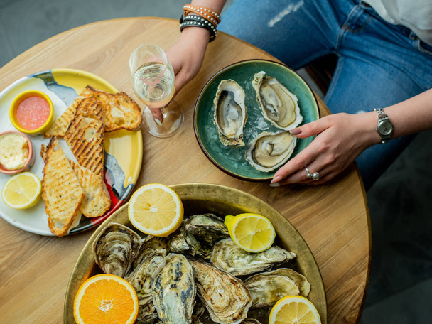 Cropped image of woman sitting at table with oysters and champagne glass - Foto, Imagen