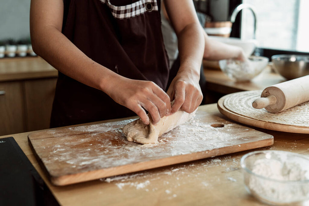 Vrouwelijke banketbakker die brood deeg kneedt op het werkblad in de keuken. Koken met bloem en boter. Hoe brood deeg te maken met de handen. Kookprocedure. - Foto, afbeelding