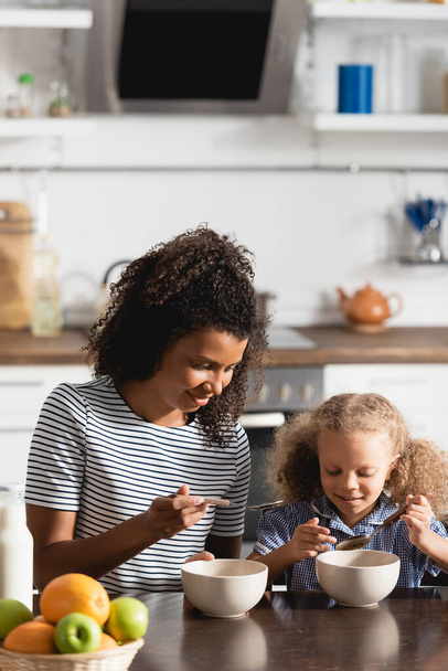 african american mother and daughter holding spoons near bowls with breakfast - Foto, Imagem