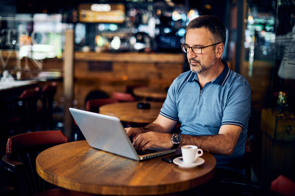 maduro adulto homem sentado no cafeteria e digitação no laptop
. - Foto, Imagem