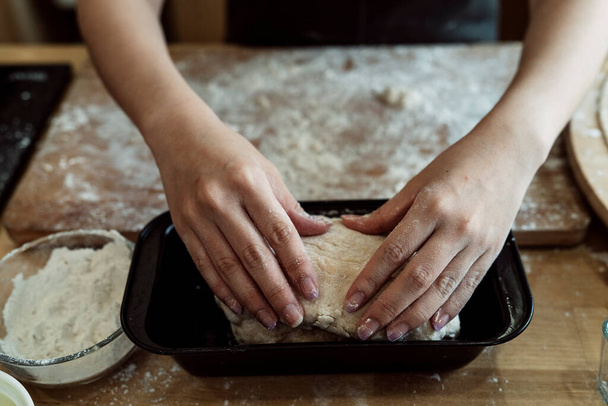 Κοντινό χέρι του σεφ ζαχαροπλαστικής βάζοντας ζύμη ψωμιού σε καλούπι πριν το ψήσιμο. - Φωτογραφία, εικόνα