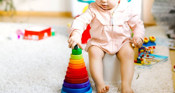 Szekrény aranyos kis 12 hónapos csecsemő kislány gyermek ül bilin. A gyerek oktató fából készült játékkal játszik. Vécéedzés. Babatanulás, fejlesztési lépések - Fotó, kép