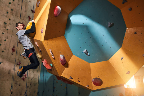 Powerful physically challenged rock-climber overhanging at hold at climbing wall - Foto, Imagem
