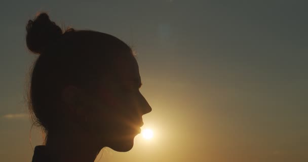 Seitenporträt von Mädchen mit Dutt küsst Sonne im Freien auf goldenem Abendlicht Hintergrund aus nächster Nähe. Schöne weibliche Profil Silhouette auf Sonnenuntergang Himmel kopieren Text Raum Zeitlupe. Glückssommer - Filmmaterial, Video