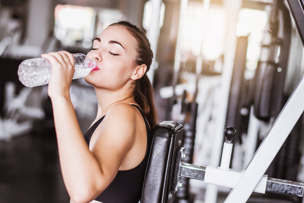Attractive young Caucasian beautiful woman get resting and drink some water from plastic bottle after workout at gym  - Valokuva, kuva