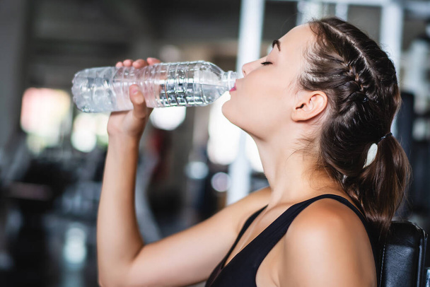 Jovem mulher bonita branca atraente obter descanso e beber um pouco de água de garrafa de plástico após o treino no ginásio
  - Foto, Imagem