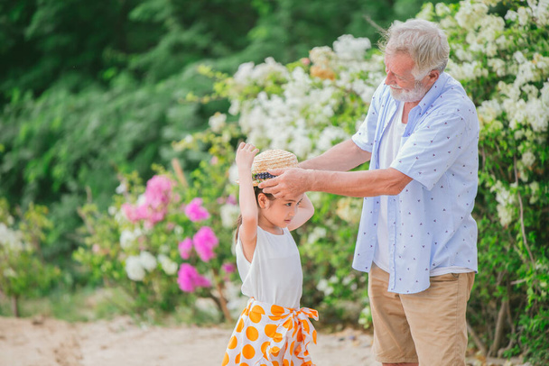 Dziadek ubrany kapelusz dla wnucząt dziewczynka podczas wakacyjnej podróży na polu kwiat parku wygląda uroczy piękny i ciepły - Zdjęcie, obraz