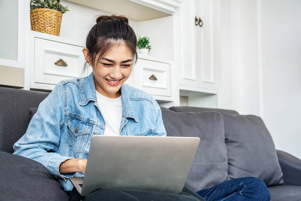 Asiática adolescente está sentada no sofá em sua própria casa conversando com seus colegas para um trabalho de projeto em um computador sobre seu trabalho na empresa
 - Foto, Imagem