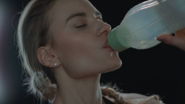 Deporte mujer beber agua de la botella de fitness sobre fondo negro - Foto, Imagen