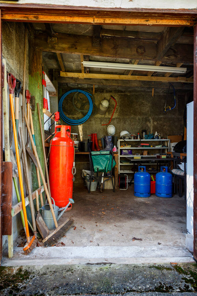 Eski bahçe aletleri ve kırmızı ve mavi gaz şişeleriyle dolu eski bir barakanın içi. - Fotoğraf, Görsel