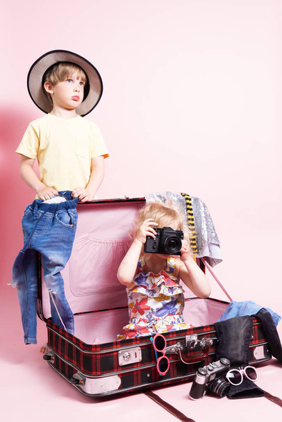 Travel: Children little boy and girl pack things in a big red suitcase for travel. The child holds in his hands a large camera. - Foto, Imagen
