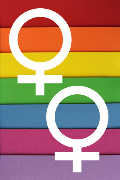 ΦΩΤΟΓΡΑΦΙΑ πολύχρωμου χαρτιού στα χρώματα της σημαίας ΛΟΑΤ δύο λευκά γυναικεία σύμβολα. Φύλλα υφής από χαρτί κόκκινο, πορτοκαλί, κίτρινο, πράσινο, μπλε, μωβ. LGBT concept, σύμβολο ΛΟΑΤ, αφίσα φόντου, - Φωτογραφία, εικόνα
