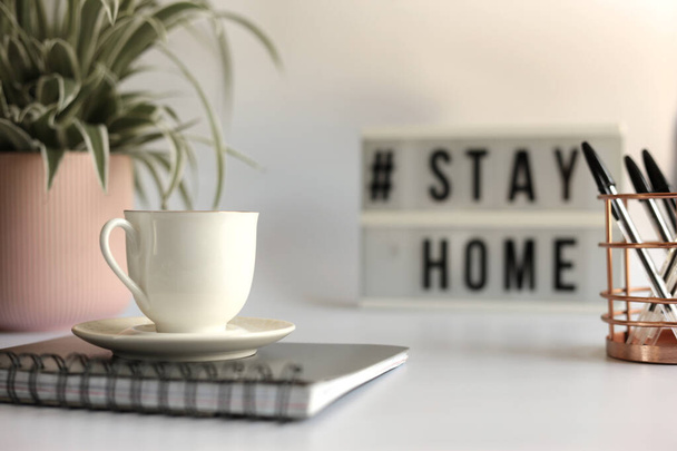 Home office desc concept during self quarantine as preventive measure against virus. Stay safe concept. Cup of coffee, clock, stationary, home plant on white background - Foto, afbeelding