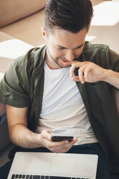 Hymyilevä valkoihoinen mies juttelemassa mobiililaitteella ja pitämässä kannettavaa polvillaan - Valokuva, kuva