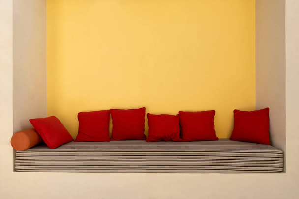 ストライプクッションマットレスと赤い柔らかい枕で快適なニッチソファを空にします。誰もいない現代的なソファは、屋外の夏のリゾートタウンに座っています。贅沢とリラクゼーションの概念. - 写真・画像