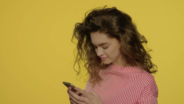 Mujer joven usando el teléfono móvil en amarillo. Mujer escribiendo mensaje en el teléfono móvil - Foto, imagen