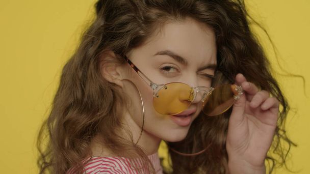 Mulher brincalhão em óculos amarelos olhando para câmera e piscar os olhos em estúdio
 - Foto, Imagem