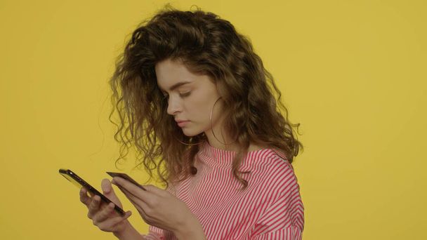 Mujer joven que utiliza aplicaciones de dinero en el teléfono inteligente para la tarjeta bancaria de pago en el estudio amarillo - Foto, Imagen