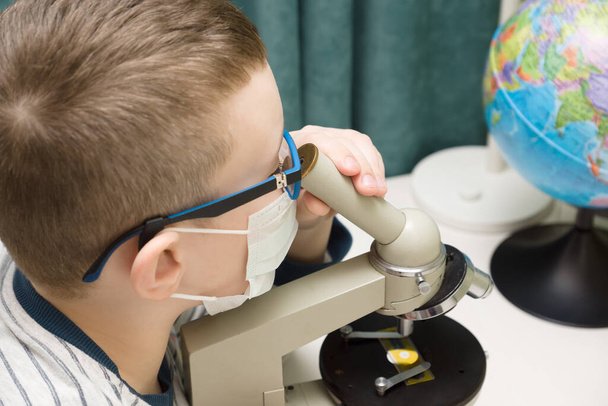 αγόρι σε μια προστατευτική μάσκα με ένα μικροσκόπιο ψάχνει για μια θεραπεία για το viru - Φωτογραφία, εικόνα