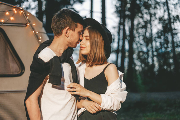 Young couple in love in stylish fashionable outfit romantic weekend wedding trip against background of camper in forest road trip - Photo, Image